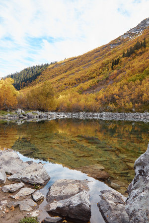 autumn landscape in mountains, lake with clear water, golden trees on slopes of mountains, stone shoreの写真素材