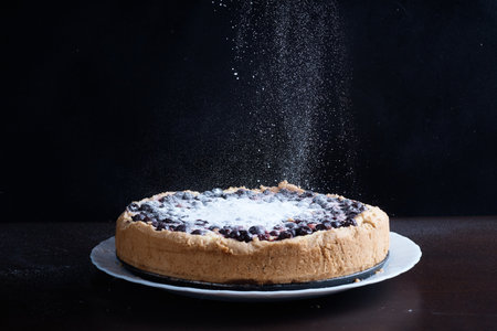 powdered sugar is sprinkled on fresh hot berry pie, cheesecake, close-up, dessert on plate, dark backgroundの写真素材