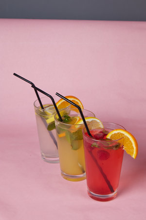 several different drinks on table, lemonade in glass, slice of lemon and straws, light background, indoorsの写真素材