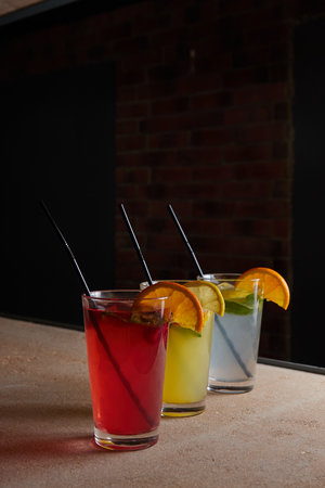 several different drinks on table, lemonade in glass, slice of lemon and straws, dark background, indoorsの写真素材