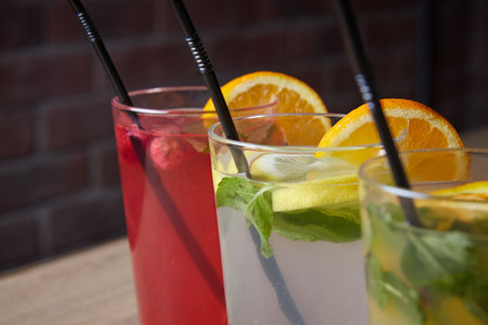 several different drinks on table, lemonade in glass, slice of lemon and straws, dark background, indoorsの写真素材