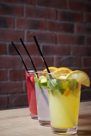 several different drinks on table, lemonade in glass, slice of lemon and straws, dark background, indoorsの写真素材