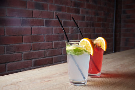 several different drinks on table, lemonade in glass, slice of lemon and straws, dark background, indoorsの写真素材