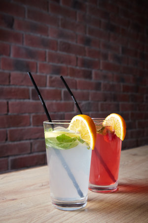 several different drinks on table, lemonade in glass, slice of lemon and straws, dark background, indoorsの写真素材