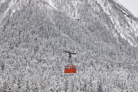pendulum lift in mountains, cable car, red cabin, winter, snow on slopes and her on forest,の写真素材