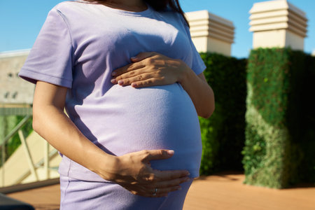 pregnant girl holding her belly, around flowers and plants, in garden