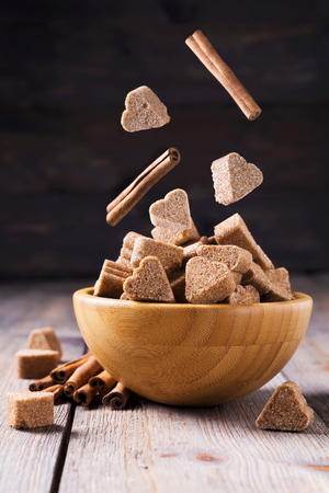 Bamboo plate with sugar flying in a heart shape and cinnamon on a dark wooden background. Selective focusの写真素材