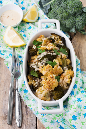 Baked cauliflower and broccoli with a sauce of tahini in a white ceramic plate on old wooden background. Selective focus.の写真素材