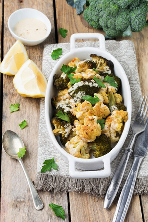 Baked cauliflower and broccoli with a sauce of tahini in a white ceramic plate on old wooden background. Selective focus.の写真素材