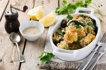 Baked cauliflower and broccoli with a sauce of tahini in a white ceramic plate on old wooden background. Selective focus.の写真素材