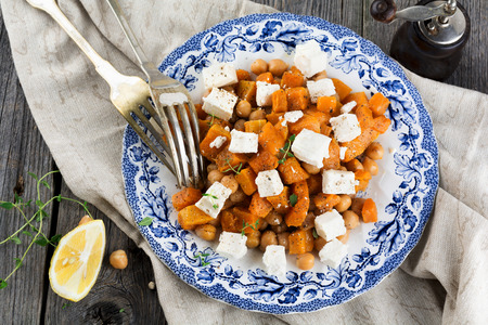 Warm salad of pumpkin, chickpeas and feta cheese on the old wooden background. Selective focus.の写真素材