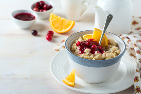  Oat porridge with cranberry sauce and orange in a ceramic bowl for healthy breakfast on a light background. Selective focus.の写真素材