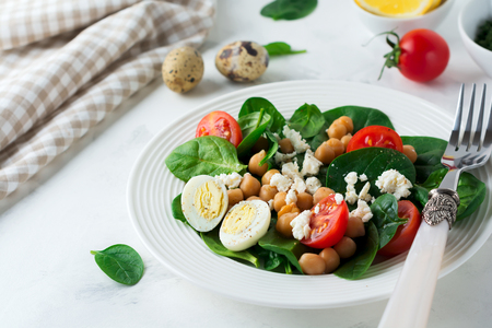 Vegetarian salad with spinach, chickpeas, cherry tomatoes, egg and Feta cheese and lemon on a light background. Selective focus.の写真素材