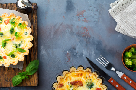 Homemade quiche tart with red fish salmon, broccoli, basil, seasonings and cheese on a gray stone...