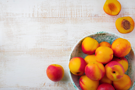 Fresh juicy fruit nectarines in ceramic bowl  on  white wooden background. Selective focus. Top view. Rustic style.の写真素材