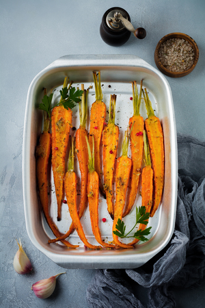 Baked carrots with spices, garlic and olive oil in a simple aluminum form on a gray concrete background. Selective focus. Top view. Rustic style.の写真素材