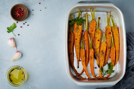 Baked carrots with spices, garlic and olive oil in a simple aluminum form on a gray concrete background. Selective focus. Top view. Rustic style.の写真素材