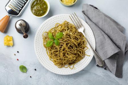 Pasta spaghetti with pesto sauce, basil and parmesan cheese on a white ceramic plate and gray concrete or stone background. Traditional Italian dish. Selective focus. Top view.の写真素材