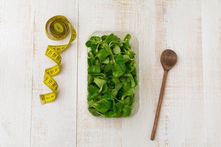 Fresh raw salad leaves in plastic box on  light wooden background. Selective focus. Top view. Copy space.の写真素材