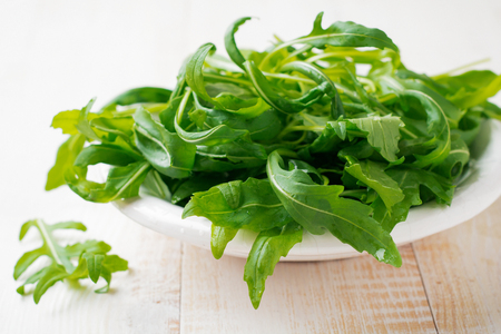 Fresh raw arugula leaves salad in  white ceramic plate on  light wooden background. Selective focus.の写真素材