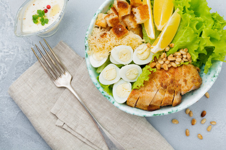 Traditional Caesar Salad with quail eggs and pine nuts in a light ceramic bowl On a gray stone or concrete background. Lunch bowl. Selective focus. Top view.の写真素材