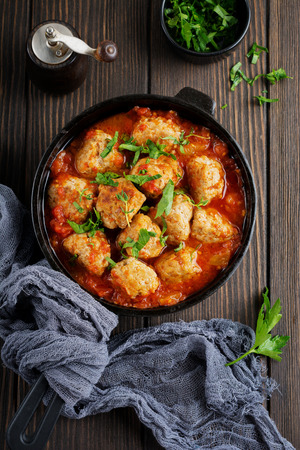 Meatballs in tomato sauce garlic and parsley in an iron frying pan on a dark brown wooden background. Selective focus. Top view. Copy space.の写真素材
