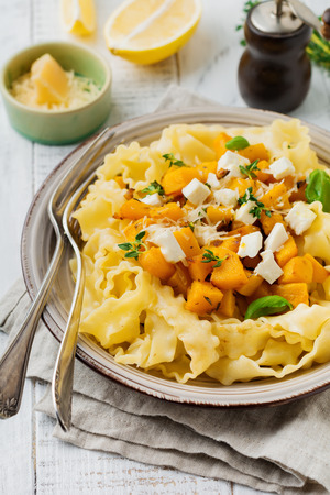 Pasta Mafaldine Napoletane with baked pumpkin, feta cheese and seasoning herbs in ceramic plate on white wooden background. Selective focus. Rustic style. Top view.の写真素材