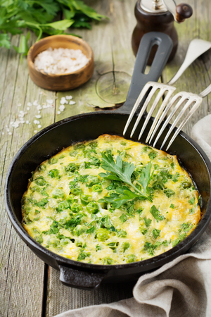 Fritatta with potatoes, green peas and herbs in an iron frying pan on an old wooden background. Selective focus. Rustic style.の写真素材