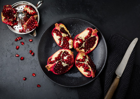 Fresh ripe pomegranate, cut into pieces on black concrete or stone background. Selective focus....