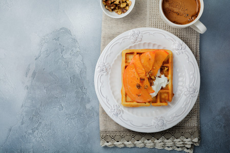 Delicious Belgian wafers with caramelized fruit, apple, banana, persimmon, pear and walnuts on a gray concrete or stone background. Ideas for breakfast. Selective focus. Top view. Place for text.の写真素材