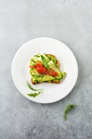 Open toast with trout, salmon, avocado, cucumber and arugula on wooden stand on gray concrete background. Selective focus. Top view. Copy spaceの写真素材