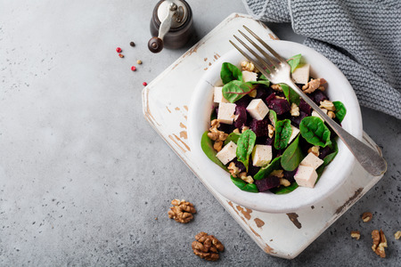 Chard, arugula, beetroot, ricotta cheese and walnut salad with olive oil in a ceramic old plate on a gray stone or concrete aged background. Selective focus. Top view. Copy space.の写真素材