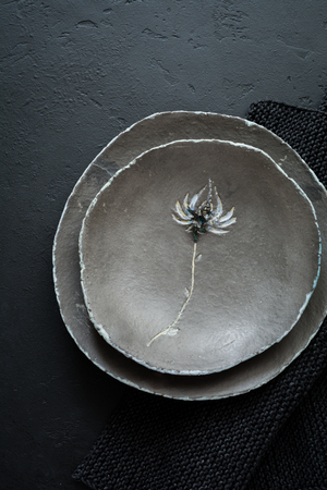 Ðmpty rustic flat plate of gray clay with beautiful flower on black concrete background. Selective focus. Top view. Copy space.の写真素材