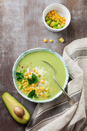 Homemade tender soup puree from avocado and corn with cream in rustic ceramic plate on gray concrete old background. Selective focus. Top view. Copy space.の写真素材