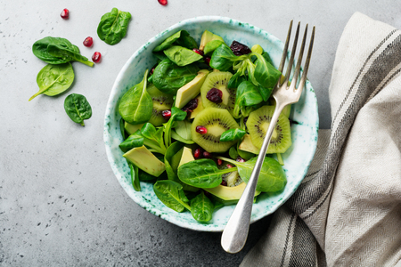 Salad of spinach baby leaves, watercress, kiwi, avocado and pomegranate in old ceramic plate on gray concrete background. Selective focus. Top view. Copy space.の写真素材
