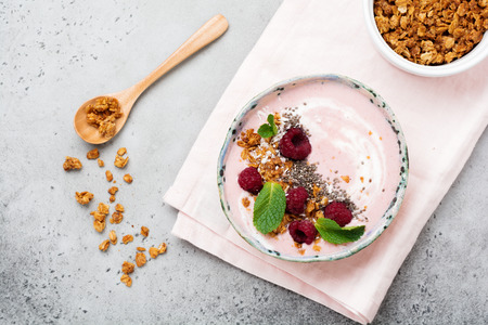 Pink raspberry banana smoothie bowl with granola, chia seeds, coconut and mint on light gray concrete background. Selective focus. Top view. Copy space.の写真素材
