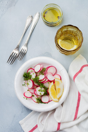 Simple salad of fresh radish with dill, lemon juice and olive oil in white ceramic bowl on light gray concrete or stone background. Selective focus. Top view.の写真素材