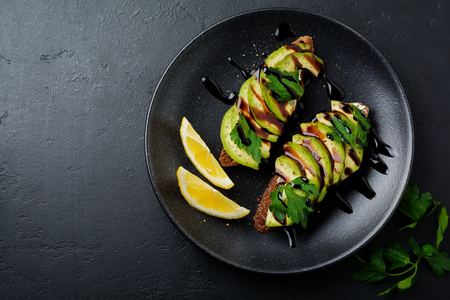 Spicy rye toasts with avocado, lemon and balsamic sauce on black concrete old background. Selective focus. Top view.の写真素材