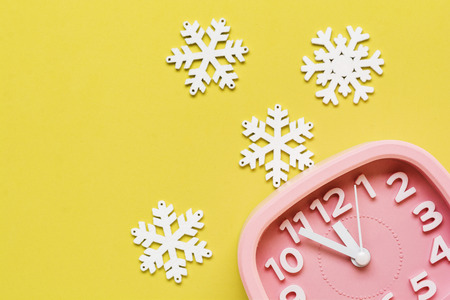 Pink alarm clock with toys and snowflakes lying on yellow surface background. New Year or Christmas concept. Top view. Cope space.の写真素材