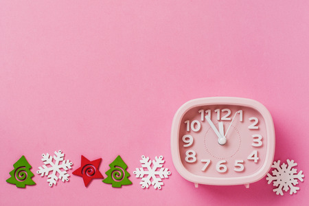 Pink alarm clock with toys and snowflakes lying on pink surface background. New Year or Christmas concept. Top view. Cope space.の写真素材