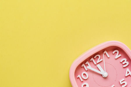 Pink alarm clock lying on yellow surface background. Top view.の写真素材
