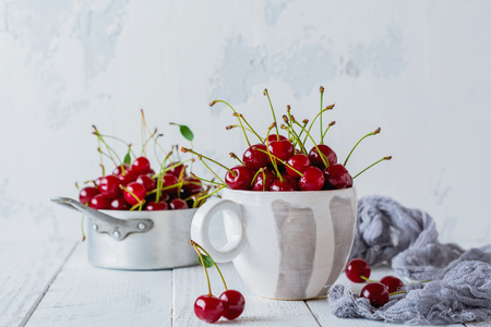 Fresh cherries in rustic aluminum saucepan on light wooden old background.の写真素材