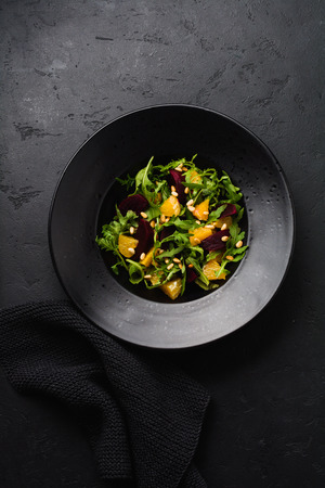 Beets, orange, pine nut, olive oil, feta cheese and arugula salad in black ceramic plate on dark concrete table background. Top view.の写真素材