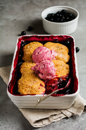 Raspberries and black currants cobbler with raspberry ice cream in baking dish. Homemade fruit pie pastries. Gray vintage background. Top view.の写真素材