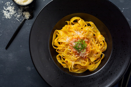 Fettuccine pasta with traditional Italian Passat sauce and parmesan cheese in black plate on dark background. Top view.の写真素材