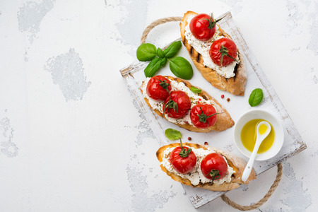 Sandwich with baked cherry tomatoes, garlic, olive oil and curd cheese on white background. Italian Cuisine. Top view.
の写真素材