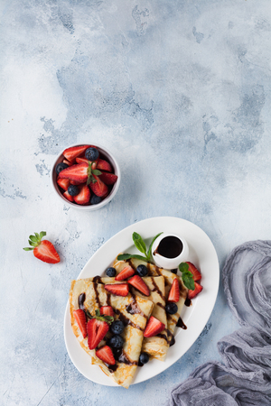 Delicious crepe with chocolate topping and fresh strawberry on white plate, top view.の写真素材
