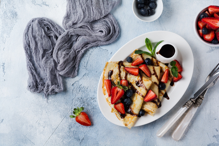 Delicious crepe with chocolate topping and fresh strawberry on white plate, top view.の写真素材