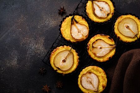Pears and custard mini tarts on a dark brown concrete old table background. Top view.の写真素材