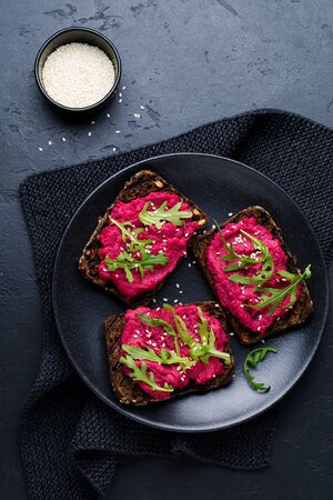 Bruschetta with beetroot hummus, arugula and sesame seeds on dark concrete background. Top view.の写真素材